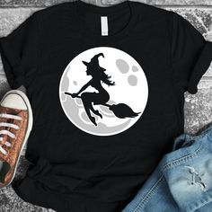 a black t - shirt with a witch flying in front of the moon