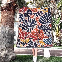 a woman standing under a palm tree holding up a colorful blanket