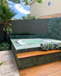 a hot tub sitting on top of a wooden bench next to a lush green plant