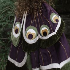 the back of a woman's purple dress with green and white feathers on it