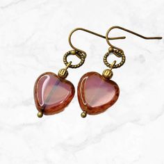 Beautiful tea rose pink Czech glass heart earrings. Picasso finish on the edges of the hearts, they dangle from small bronze rings. Elegant earrings that work for everyday wear or dressed up. Lightweight and comfortable. So pretty, this earring's color works well with pink, brown, beige, blue, green and more. Great with denim.  Hypoallergenic ear wires (nickel and lead free). Choose ear wire style at checkout. Artisan glass heart beads produced in small quantities in the Czech Republic.  Free Gi Heart Beads Metal Earrings For Gift, Metal Heart Beads Earrings For Gifts, Metal Heart Beaded Earrings For Gifts, Vintage Double Heart Earrings For Gift, Vintage Double Heart Earrings As Gift, Handmade Vintage Metal Heart Earrings, Gift Metal Heart Earrings With Heart Beads, Pink Heart-shaped Glass Jewelry, Heart-shaped Pink Glass Jewelry