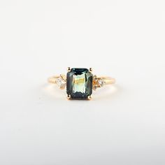 a ring with an emerald colored stone surrounded by three white diamonds on a white background