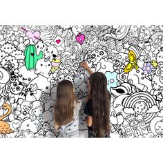 two girls standing next to each other in front of a wall with cartoon drawings on it