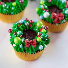 three cupcakes decorated with green and red decorations on top of a white table