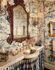 a bathroom with blue and white wallpaper has a large mirror above the sink in front of it