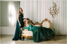 two women in green dresses are posing for the camera while sitting on an ornate couch