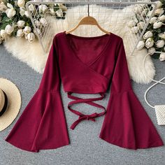 This elegant burgundy blouse features a unique and stylish design perfect for a modern wardrobe. The deep, rich shade of red gives it a luxurious feel, while the soft, velvety fabric adds a touch of sophistication. Its long, bell sleeves provide a dramatic flair, complementing the wrap-style front that creates a flattering V-neckline.The blouse cinches at the waist with a matching fabric belt, off.. Types Of Crop Tops Names, Wrap Top Outfit Classy, Long Sleeve Top Outfit, Blusas Top, Bandage Crop Top, Shirt Elegant, Bell Sleeve Crop Top, Bodycon Tops, Flare Long Sleeve