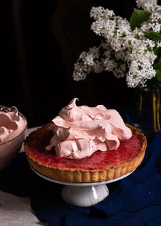 there is a pie with whipped cream on it next to a bowl full of flowers