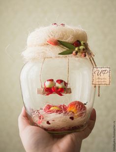 a hand holding up a glass jar filled with fake flowers and birds in it's nest