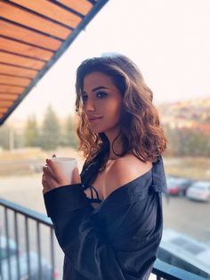 a woman is holding a coffee cup and looking off to the side while standing on a balcony