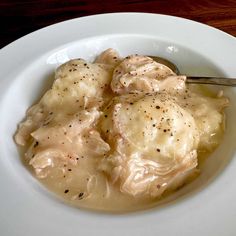 a white plate topped with dumplings covered in gravy next to a fork