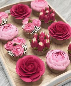 cupcakes decorated with pink frosting and flowers on a wooden tray, ready to be eaten