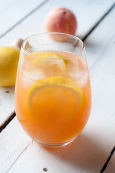 a glass filled with liquid next to two lemons and an apple on a table