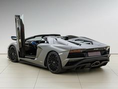 a silver sports car with its doors open in a room that has white tiles on the floor