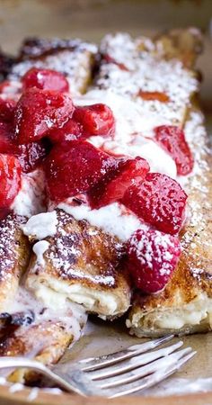 french toast with strawberries on top and powdered sugar over the top, served with a fork