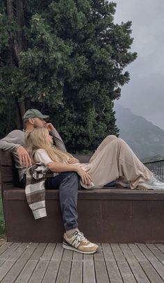 a man and woman sitting on a bench next to each other with trees in the background