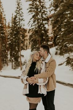 a man and woman standing in the snow with their arms around each other as they hug