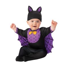 a baby wearing a bat costume sitting on the floor with his hands in the air