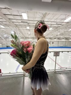 a woman in a black dress is holding flowers and looking at an ice skating rink