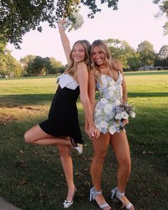 two beautiful young women standing next to each other in front of a tree and grass field