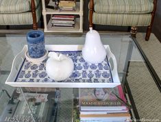 a glass table topped with a tray filled with books and vases on top of it