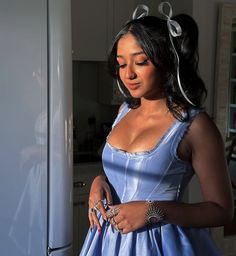 a woman in a blue dress standing next to a white refrigerator with her hands on her hips