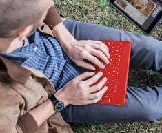 a man sitting in the grass using a red laptop computer with his hands on it