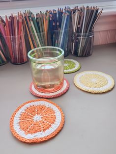 three crocheted coasters with an orange and white design on them next to a cup of water