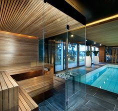 an indoor swimming pool surrounded by glass walls and wooden steps leading to the upper level