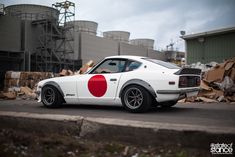 a white car with a red circle painted on it's side parked in front of a pile of junk