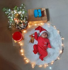 a baby laying on top of a white rug next to christmas lights and presents under a tree