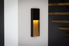 a wall mounted light on the side of a white wall next to some wooden steps