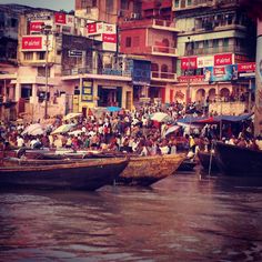 many people are sitting on boats in the water near some buildings and stores with umbrellas over their heads