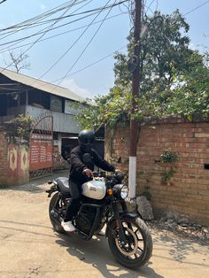 a man riding on the back of a motorcycle down a street next to a brick building