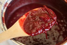 a wooden spoon filled with red sauce on top of a pot