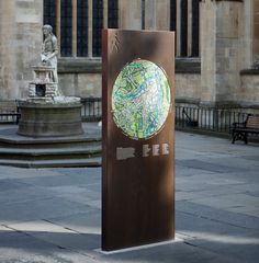 a metal sign with a map on it in front of a stone building and fountain