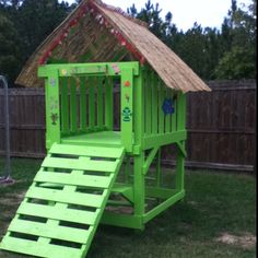 a green wooden play set with stairs and a straw hut on it's roof