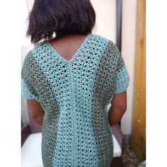 a woman wearing a green crochet sweater standing in front of a white wall