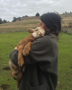 a woman holding a baby goat in her arms on top of a lush green field