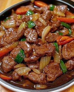 beef and onions with peppers in a bowl on a wooden table top, ready to be eaten