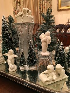 a glass table topped with figurines next to a vase filled with snow covered trees