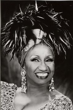 a black and white photo of a woman with feathers on her head smiling at the camera