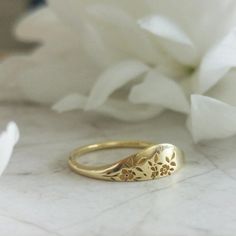 a close up of a gold ring on a marble surface with flowers in the background