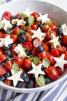 a white bowl filled with tomatoes, blueberries and star shaped salad dressing on top of a striped cloth