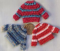 three crocheted sweaters and a penny on a white tablecloth with blue, red, and white stripes