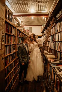 the bride and groom are standing in front of bookshelves with ladders to reach them