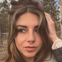 a woman with long hair and piercings on her nose looking at the camera while standing in front of a fence