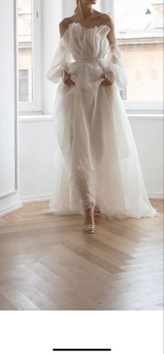 a woman standing in front of a window wearing a white dress with ruffles