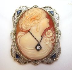 "This is a beautiful and very unique cameo piece. I'm estimating that this is from around the 1920's. This frame of this piece is a very ornately carved 14k gold rectangular shape with scalloped edges. The piece is made of carved out filigree patterns with four triangle shaped blue Spinel stones set, one in each corner. There is a strand of seed pearls that are strung on wire and completely surround the center shell Cameo. The cameo features a woman looking to the side. Her hair is up in a soft Collectible Art Deco Carved Jewelry, Art Deco Carved Collectible Jewelry, Ornate Cameo Jewelry For Vintage Events, Collectible Art Deco Cameo Jewelry, Art Deco Cameo Jewelry For Formal Occasions, Art Deco Cameo Jewelry As A Gift, Art Deco Cameo Jewelry For Anniversary, Art Deco Wedding Jewelry With Cameo, Diamond Drop Necklace