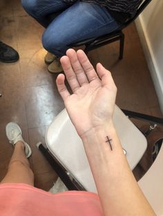 a person sitting in a chair with their hand up to the cross on her wrist